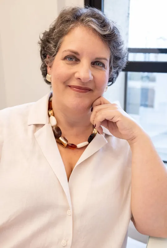Dra. Patrícia Barros, de camisa clara e colar de contas, sorri com a mão apoiada no rosto.